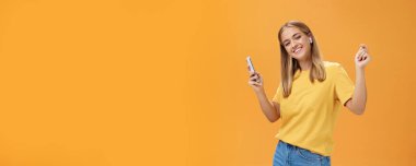 Kablosuz kulaklık takan neşeli Avrupalı kadın. Elinde akıllı telefon kulaklığı, kaldırılmış ellerle dans ediyor. Mutlu bir gülümseme.