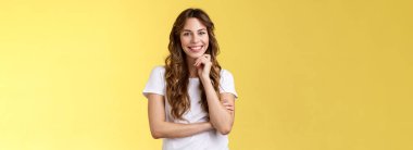 Şefkatli, şevkli, çekici Avrupalı kadın uzun kıvırcık saçlı, komik bakışlı, sırıtan, neşeli, dokunaklı çene hareketli, meraklı, meraklı, meraklı, neşeli, sarı arka planı dinleyen..