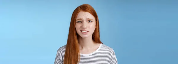 Displeased young awkward redhead girl cringe full disbelief smirking frowning confused look questioned doubtful hearing nuisance dumb story standing blue background uncertain. Copy space