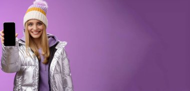 Yaşam tarzı. Dost canlısı, kendine güvenen, güler yüzlü, kendine güvenen sarışın kız. Şık kış şapkalı. Kolunu uzat ve akıllı telefon reklamını göster.