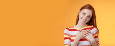 Sevinçli, kadınsı, güzel, kızıl saçlı bir kadın iltifat kabul ediyor. Dokunuyor, dokunuyor, gülümsüyor, seviniyor, gülümsüyor, sevgi dolu, turuncu arka planda duruyor..