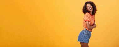 Takılmak ister misin? Şehvetli ve cilveli, tasasız, stil sahibi, esmer, kıvırcık saçlı, profil çizen, sola dönüp mutlu bir ifadeyle gülümseyen ve turuncu duvarın üzerinde baştan çıkaran bir kadın..