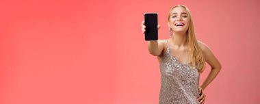 Neşeli, neşeli, neşeli, neşeli, Avrupalı, şık, parlak, parlak elbiseli, el ele tutuşan, kendine güvenen, kollarını uzat. Akıllı telefon ekranını göster. Yeni uygulama cihazı, kırmızı arka plan..