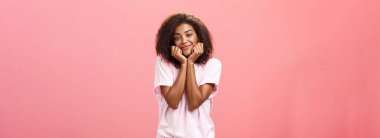 Hayalperest Afro-Amerikalı kız arkadaş kıvırcık saç stili iç çekiyor, avuçlarına yaslanıyor ve nazikçe gülümsüyor sanki sevgilisini hayal ediyor ya da ona karşı bir şeyler hissediyormuş gibi.