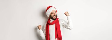 Kış tatili ve yeni yıl partisi konsepti. Noel Baba şapkalı yakışıklı sakallı adam, amacına ulaş ve kutla, yumruk salla ve evet de, beyaz arka plan.