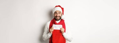 Kış tatili ve alışveriş konsepti. Heyecanlı yakışıklı adam yeni yılı planlıyor, elinde hediyeler için Noel çorabı tutuyor ve düşünüyor, beyaz arka planda duruyor..