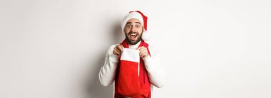 Kış tatili ve kutlama konsepti. Şaşırmış sakallı adam Noel çorabının içine bakıyor, yeni yıl hediyesi alıyor, beyaz arka planda duruyor..