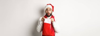 Kış tatili ve kutlama konsepti. Şaşırmış sakallı adam Noel çorabının içine bakıyor, yeni yıl hediyesi alıyor, beyaz arka planda duruyor..