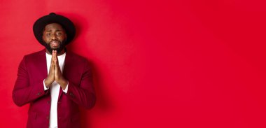 Sefil siyah adam yardım istiyor, yardım dileniyor, üzgün görünüyor, kırmızı arka planda duruyor. Boşluğu kopyala