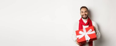 Kış tatili kavramı. Gülümseyen adam sana bir hediye veriyor, hediyesini tutuyor ve mutlu Noeller diliyor, beyaz arka planda duruyor..