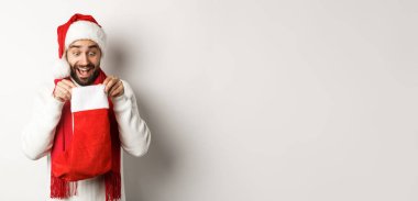 Kış tatili ve kutlama konsepti. Mutlu adam Noel çorabının içine bakıyor, yeni yıl hediyesi alıyor, beyaz arka planda duruyor..