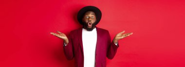 Noel alışverişi ve insanların konsepti. Yakışıklı afro-amerikan adam şaşırmış, ellerini yana açmış, tanıtım tekliflerini fotokopi alanında, kırmızı arka planda gösteriyor..