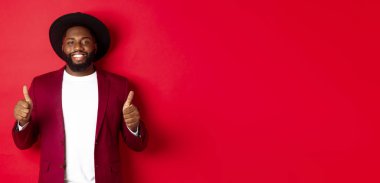 Noel alışverişi ve insanların konsepti. Yakışıklı siyah adam tatmin olmuş gülümsüyor, onaylıyor ve onaylıyor, kırmızı arka planda duruyor..