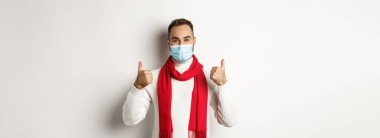 Covid-19, tecrit ve karantina konsepti. Yüz maskesi takan gülümseyen ve baş parmağını kaldıran, kendini koronavirüsten koruyan, beyaz arka planda duran.