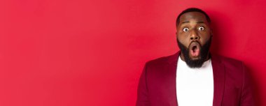 Şok olmuş, soluk soluğa kalmış, çenesi düşmüş, kameraya bakan, kırmızı arka planda duran siyahi adamın yakın çekimi..