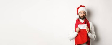 Kış tatili ve alışveriş konsepti. Noel Baba şapkalı yakışıklı adam hediyeleri düşünüyor, Noel çorabı tutuyor, beyaz arka planda dikiliyor..