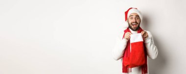 Kış tatili ve kutlama konsepti. Şaşırmış sakallı adam Noel çorabının içine bakıyor, yeni yıl hediyesi alıyor, beyaz arka planda duruyor..