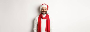 Noel tatili. Noel Baba şapkası ve kırmızı eşarplı gülümseyen sakallı adam, mutlu gülümsüyor, beyaz arka planda duruyor..