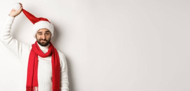 Noel partisi ve kutlama konsepti. Üzgün adam Noel Baba şapkasını çıkarıp yüzünü buruşturuyor, üzgün görünüyor, beyaz arka plana karşı duruyor, kötü yeni yıl.