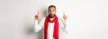Noel alışverişi ve kış tatili konsepti. Şaşırmış sakallı adam yeni yıl tanıtım teklifini kontrol ediyor, işaret ediyor, yukarı bakıyor, beyaz arka plana karşı duruyor..