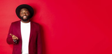 Yakışıklı gülümseyen siyah adam seni tebrik ediyor, kameraya gururla el kaldırıyor, övgüler yağdırıyor, kırmızı arka planda duruyor..