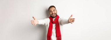 Noel tatili ve kutlama konsepti. Dost canlısı bir adam içeri girmeye davet ediyor, elini uzatıp selamlıyor ya da jestlere sarılıyor, mutlu yıllar diliyor, beyaz arka planda duruyor..