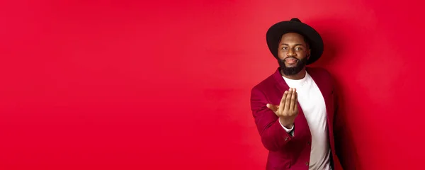 Handsome and masculine Black man asking come closer, luring to step forward, calling for you, standing over red background.