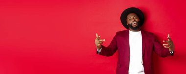 Noel alışverişi ve insanların konsepti. Kendine güvenen ve küstah bir adam jestle dans ediyor, hip hop yapıyor ve kamera karşısında kendinden emin, kırmızı arka planda..