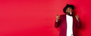 Noel ve insanlar kavramı. Mutlu siyah adam yeni yılı kutluyor ve dans ediyor, parti kıyafeti giyiyor, kırmızı arka plan.