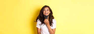 Covid-19 kavramı, sosyal mesafeler ve yaşam tarzı. Güzel bir Afro-Amerikan kızı tasviri. Yüzündeki maskeyi çıkardıktan sonra mutlu bir şekilde nefes alıyor. Gülümsüyor..