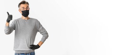 Covid-19, salgın hastalık ve sosyalleşme konsepti. Siyah tıbbi maskeli ve lastik eldivenli orta yaşlı bir adamın portresi, iyi bir şeyi onaylıyor ya da onaylıyor..