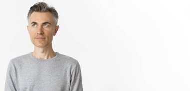 Gri kazaklı yakışıklı orta yaşlı adamın yakın çekimi, sol üst köşeye bakıyor, beyaz arka planda duruyor..