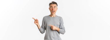 Şaşırmış orta yaşlı, gülümseyen ve parmaklarını logoya ya da reklam panosuna gösteren beyaz arka planda şaşkın duran yakışıklı bir adamın görüntüsü..