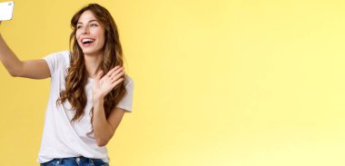 Dost canlısı, hoş görünümlü, neşeli, bayan, kol kola, akıllı telefon kaydı video blogu, kameranın önünde gülümseyen, konuşan hayranlar, selfie sarısı arka plan görüntülerini alıyor.