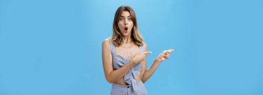 Etkileyici ve şaşırmış, güzel, kestane rengi saçlı, şirin elbiseli, heyecanlı ve şaşkınlıktan ağzı açık, mavi arka planda kalmış güzel bir kadın. Reklam.