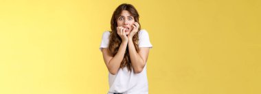 Korkmuş, korkmuş, ürkek, tırnak yiyen, kameraya bakan, korkudan titreyen, titreyen dişleri olan, korkudan titreyen, kendine güveni olmayan, sarı arka planda duran bir kız..