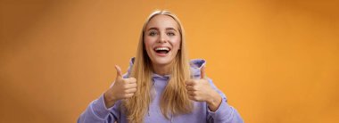 Destekleyici, sevimli sarışın kız arkadaş ilginç bir konseptten hoşlanıyor güzel fikir başparmaklar büyük ölçüde kabul ediyor kıyafet alışverişini birlikte onaylıyor, yeni bir görünüş tavsiye ediyor, turuncu arka plan.