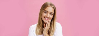 Cilt bakımı, güzellik ve cilt bakımı. Çekici ve beyaz tişörtlü beyaz bir kız saçlarına dokunuyor ve başını yana eğiyor. Aynada makyajsız kendine bakmaktan keyif alıyor..