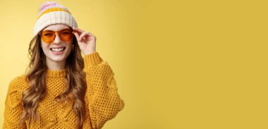 Arkadaş canlısı görünümlü, cana yakın, çekici bir kız neşe içinde gülüyor eğlenceli sohbetler ediyor güneş gözlüklerini kontrol ediyor kayak merkezini kontrol ediyor dinlenirken eğleniyor arkadaşlar, sarı arka plan.