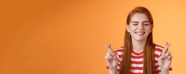 Umut dolu iyimser, neşeli, kızıl kız hayalin gerçekleştiğine inanıyor, kapalı gözler şans diliyor, dilek tutuyor, olumlu bir şans bekliyor, turuncu arka planda duruyor, gülümsüyor ve hayal kuruyor..