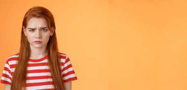 Kapalı kapılar ardında üzgün, çocuksu kızıl saçlı bir kız, suratını asıyor, üzgün, şikayet ediyor, hayal kırıklığına uğruyor, surat asıyor, huzursuz turuncu arka planda duruyor, sızlanıyor..