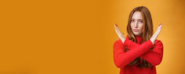 Kendine güvenen, kızıl saçlı, çilli, çapraz kollu çekici bir kadının kapalı çekimleri ve yasaklama jestleri turuncu duvarın üzerinde kendinden emin durmasını engelliyor. Vücut dili