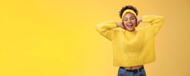 Kaygısız genç, çekici, Afro-Amerikalı. Kız ellerini başının arkasına koyup dinleniyor tembellik ediyor boş günlerin tadını çıkarıyor gülümsüyor ve boş zamanlarını sarı arka planda eğlenerek geçiriyor..