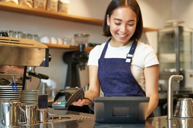 Gülümseyen Asyalı barista kız işlem sırası, POS terminaline girin, kahve dükkanında tezgahta çalışın..