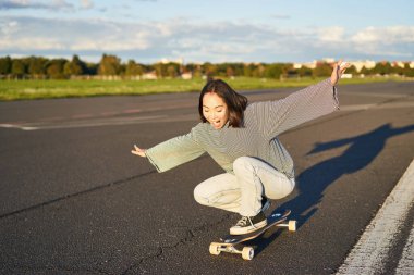 Özgürlük ve mutluluk. Mutlu Asyalı kız boş güneşli bir yolda sörf yapıyor, gülüyor ve gülümsüyor, kaykay yapıyor..
