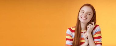 Mutlu, romantik, genç, narin kızıl kız hayal gücü yaratıyor. Gülümsüyor, seviniyor, saçlara dokunuyor, güzel anıları anımsıyor, turuncu arka planda duruyor..