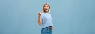 Yaşam tarzı. Çekici, sosyal ve arkadaş canlısı, sarı saçlı, sağdan dönen, gevşek ve kaygısız bir şekilde konuşan, mavi arka planda poz veren bir kadın.