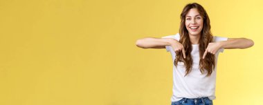 Neşeli, neşeli, neşeli, neşeli, komik, uzun, güzel saçlar, işaret parmaklarını gösteren alt promosyon, gülen, olumlu duygular paylaşan, ürün reklamcılığı sarı arka planı öneren, neşeli, neşeli, neşeli bir kız..