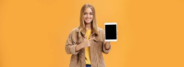 Yeni dijital tabletle sonbahar señine hazır olun. Kadife ceketli çekici bir kadının portresi cihaza bakan alet ekranını gösteriyor ve turuncu duvarın üzerinden mutlu ve dostane bir şekilde gülümsüyor.