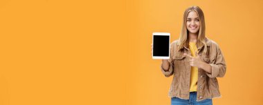 Yeni dijital tabletle sonbahar señine hazır olun. Kadife ceketli çekici bir kadının portresi cihaza bakan alet ekranını gösteriyor ve turuncu duvarın üzerinden mutlu ve dostane bir şekilde gülümsüyor.